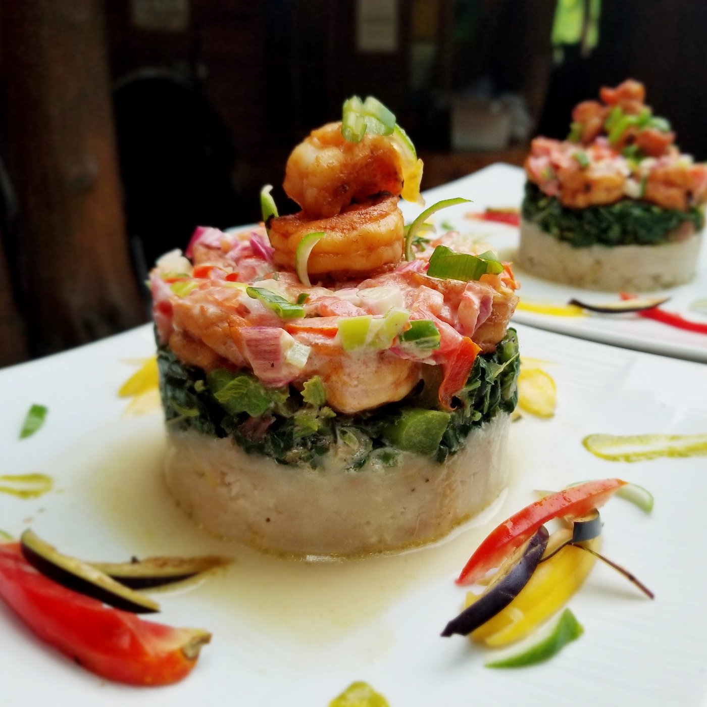 A stacked plated course of pepper shrimp over callaloo and yam, garnished with scallion and scotch bonnet ribbons.